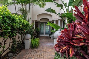 A paved pathway leading to a building entrance, surrounded by lush greenery and decorative stones. - Islands at Mauna Lani Ocean View 4-Bedroom | Car Incl. w/ 6+ Nights | ML-4220 by KBM (Waimea)