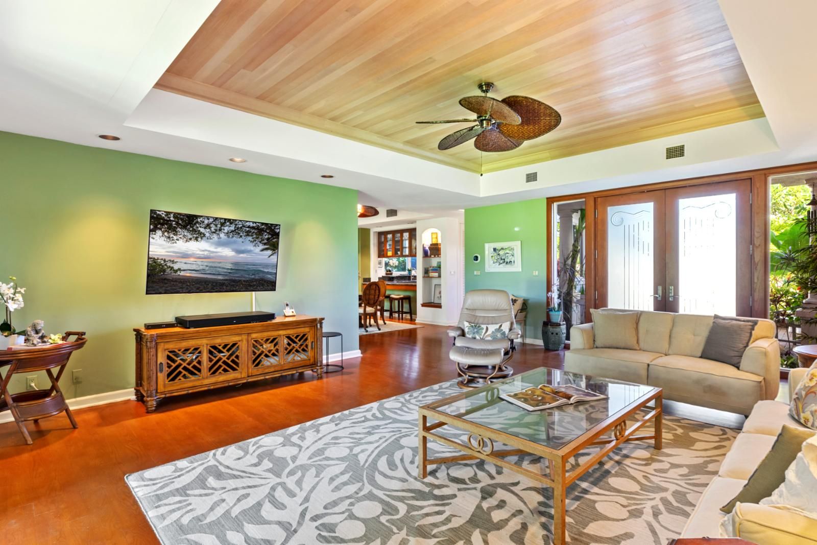 Un salón amplio con techo de madera, un televisor de pantalla plana grande, una mesa de centro de vidrio y un sofá color beige.