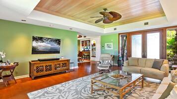 Un salón amplio con techo de madera, un televisor de pantalla plana grande, una mesa de centro de vidrio y un sofá color beige.
