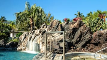 Un espace piscine agrémenté d’une cascade, entouré de rochers et de palmiers.