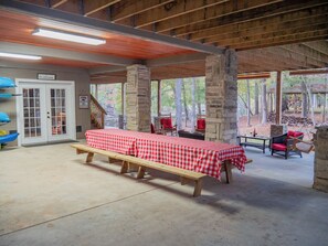 Un espacio comedor al aire libre con techo, mantel a cuadros, pilares de piedra y bancos de madera.
