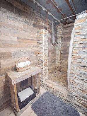 A shower area with stone walls, a wooden bench with a basket, and a grey rug. - Big Cypress Lodge on the Santa Fe River-Sleeps 14, Bring horses, RV and boat! (Fort White)