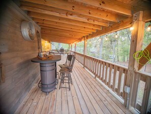 A wooden deck with a bar area, chairs, and a view of trees.