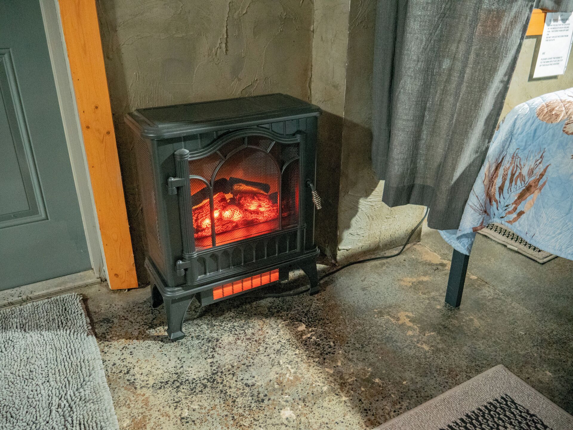 Ein Kaminofen in einem Raum mit Betonboden, einer Tür und einem Tisch mit einer Tischdecke.