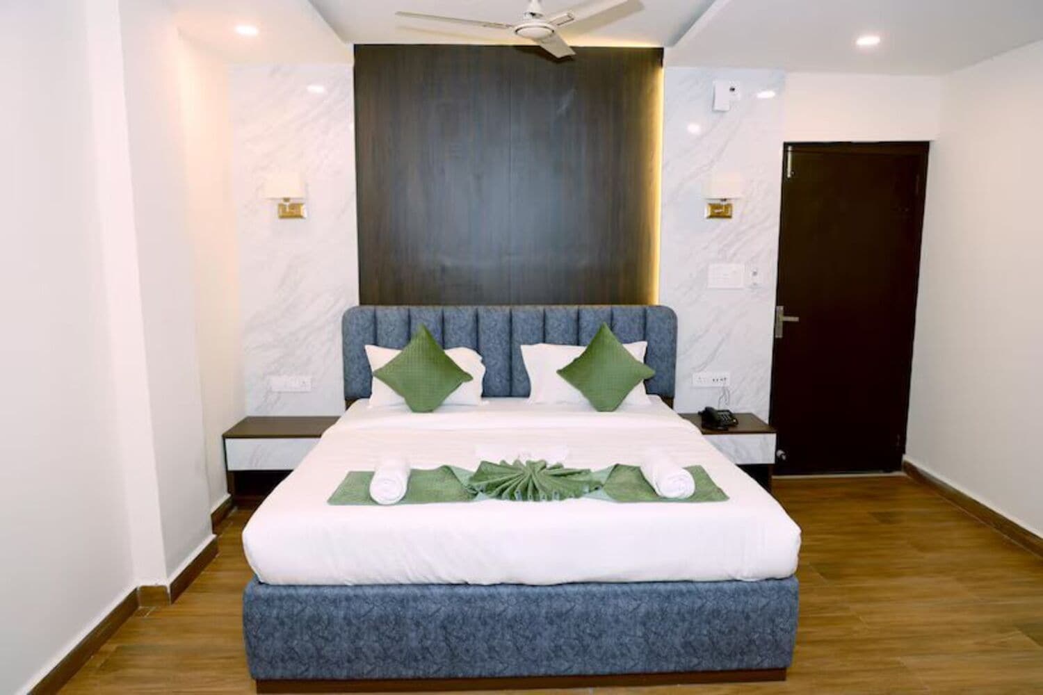 Quarto de hotel moderno com uma cama grande, um ventilador de teto e uma porta de madeira escura.