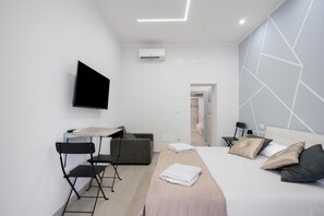 A modern hotel room with a bed, a desk, a chair, a TV, and an air conditioning unit. - Holiday Home 'La Casetta 21' with Wi-Fi and Air Conditioning (Bari)
