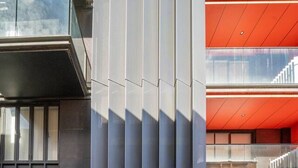 Een modern gebouw met een rode en grijze gevel, een duidelijke ingang en een trap naar een hoger niveau.