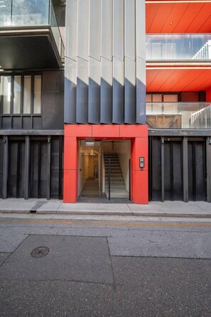 A modern building with a red and grey facade, a visible entrance, and a staircase leading to an upper level. - Koala Stay | Your Cozy City Home with WiFi (Adelaide)