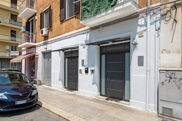 A building with two closed garage doors, a security camera, and a 'WELCOME' mat outside. - Holiday Home 'La Casetta 23' with Wi-Fi and Air Conditioning (Bari)