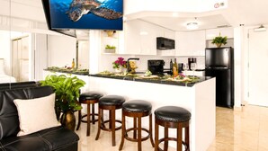 A modern kitchen with a central island, bar stools, and a flat-screen TV mounted above the island. - Ilikai | Ocean View 2 BR Sleeps 8 | Car Incl. w/ 6+ Nights | ILK ML-4241 by KBM (Honolulu)