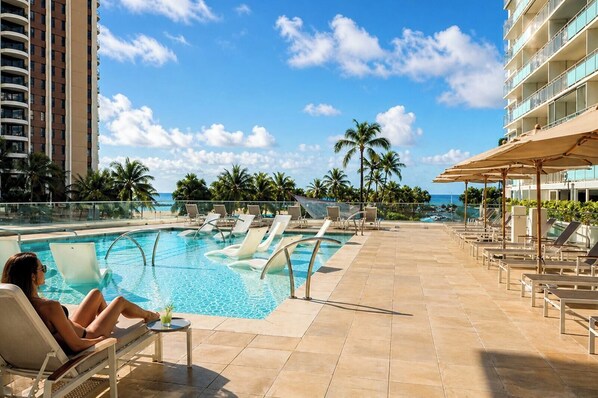 Ein Poolbereich mit Liegestühlen und einem Pool, umgeben von Palmen und wolkenlosem Himmel.