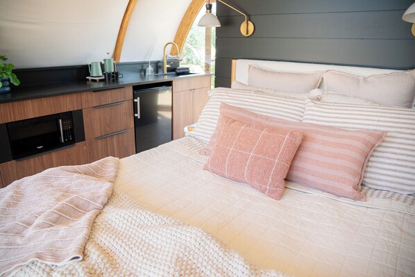 A cozy bedroom with a bed, pillows, a bedside table, a lamp, and a view of the outdoors.