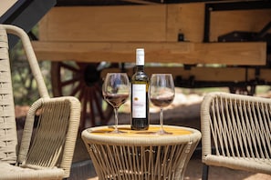 A wicker table with a bottle of red wine and two glasses on it, surrounded by wicker chairs. - Nomad Wagon With Private Hot Tub and Grill (Dripping Springs)