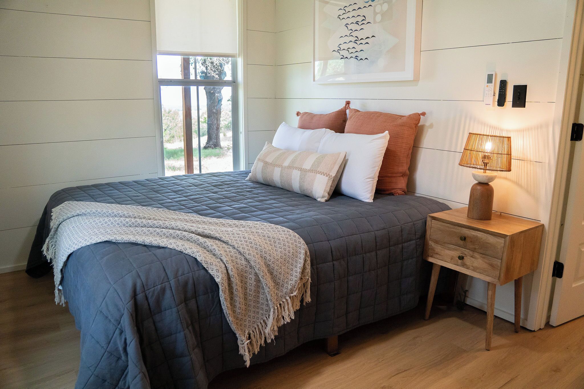 A bedroom with a bed, bedside table, lamp, and a window with a view.