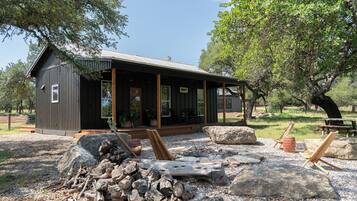 Eine rustikale Holzhütte mit Veranda, großen Steinen und Holzscheiten.