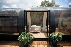 Eine transparente, gebogene Struktur mit Sitzgelegenheiten im Inneren, darunter ein Sofa und ein kleiner Tisch.