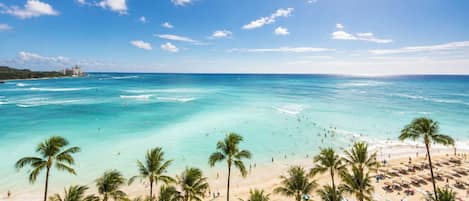 A beach with clear turquoise waters, palm trees, and beach umbrellas.