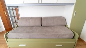 Cama verde com duas almofadas e chão de madeira.