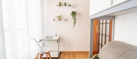 Un espacio habitable minimalista con un escritorio blanco, una silla blanca, un sofá y suelo de madera.