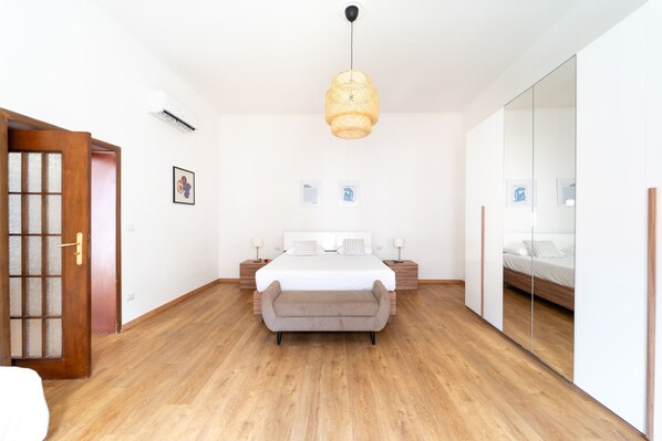 A bedroom with a bed, bedside tables, a hanging light fixture, a wardrobe, and a door. - Appartamento in Piazzetta by Wonderful Italy (Naples)