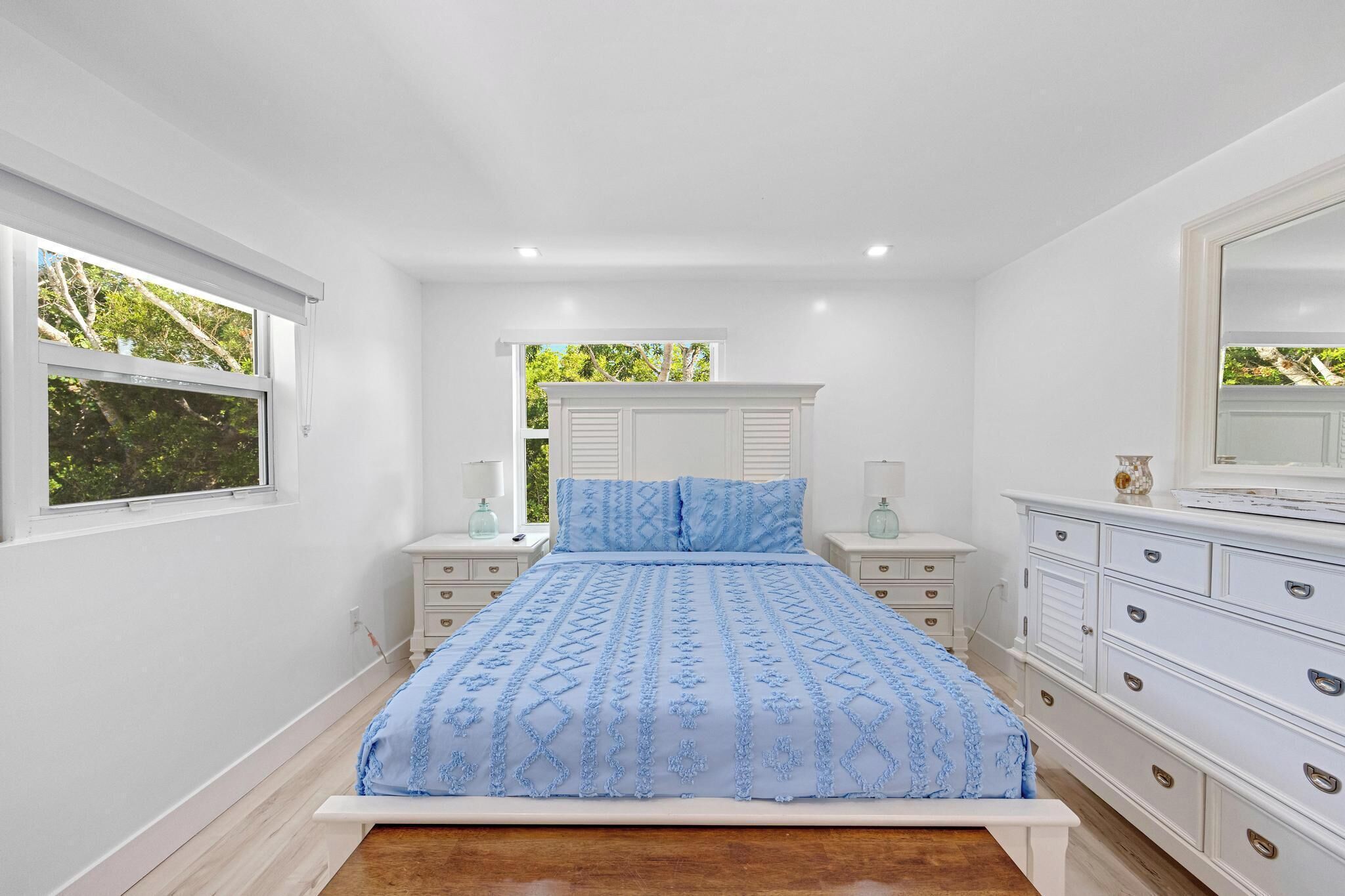 A bedroom with a bed, nightstands, a dresser, and a window with a view of greenery.