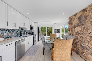 A modern kitchen with white cabinets, a stone accent wall, and a dining area with wicker chairs. - Hidden Keys Paradise-Where the Key Deer Roam-75’ Private Dock! Boaters Paradise! (Big Pine Key)