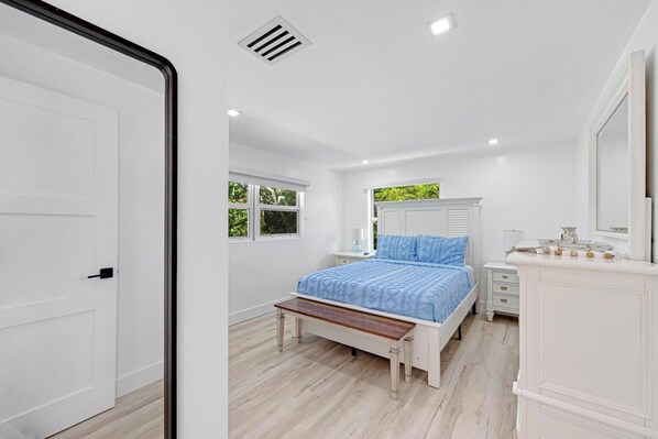 A bedroom with a bed, bedside table, dresser, and a window.