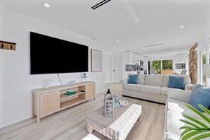 A modern living room with a flat-screen TV, a sofa set, a wooden cabinet, and a woven coffee table.