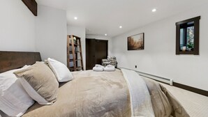 Un dormitorio con cama, almohadas, una escalera, una silla, un cuadro y una ventana.