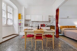 Una cocina compacta con armarios blancos, un microondas rojo y una pequeña mesa de comedor con sillas.