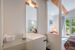 A modern bathroom with a large mirror, a white sink, and a window with a view of greenery.