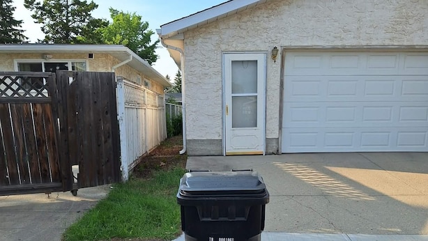 A black trash bin in front of a residential garage with a white door. - Snow's family friendly backyard oasis. YEG Airport. (Leduc)