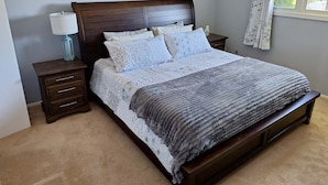 A bedroom with a wooden bed, a nightstand with a lamp, and a window with curtains. - Snow's family friendly backyard oasis. YEG Airport. (Leduc)