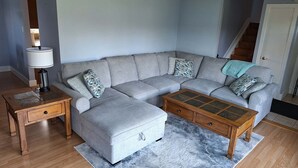 A living room with a grey sectional sofa, a wooden coffee table, a lamp, and a rug. - Snow's family friendly backyard oasis. YEG Airport. (Leduc)