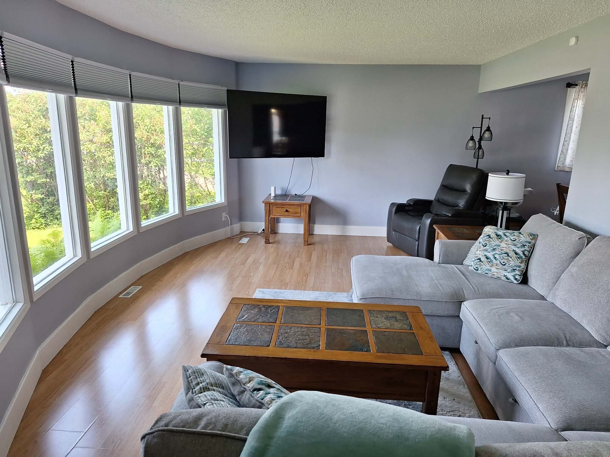 A living room with a large window, a flat-screen TV, a leather recliner, and a patterned coffee table.