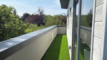 A modern balcony with a concrete edge, a glass door, and a view of greenery.