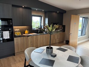 Une cuisine moderne avec des meubles de couleur sombre, un îlot central et un coin repas comprenant une table ronde et des chaises.