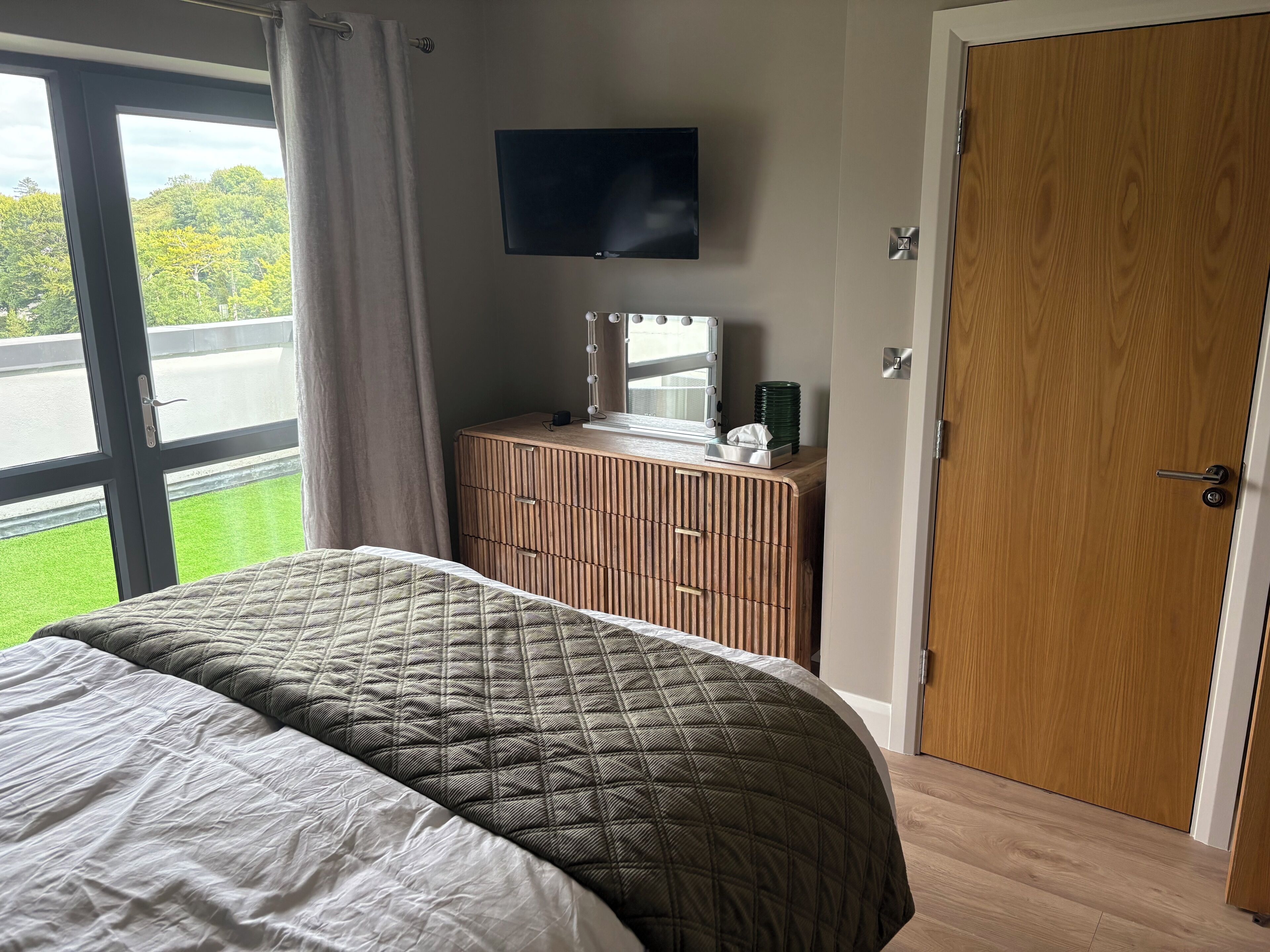 Een slaapkamer met een bed, een dressoir, een televisie en een deur.