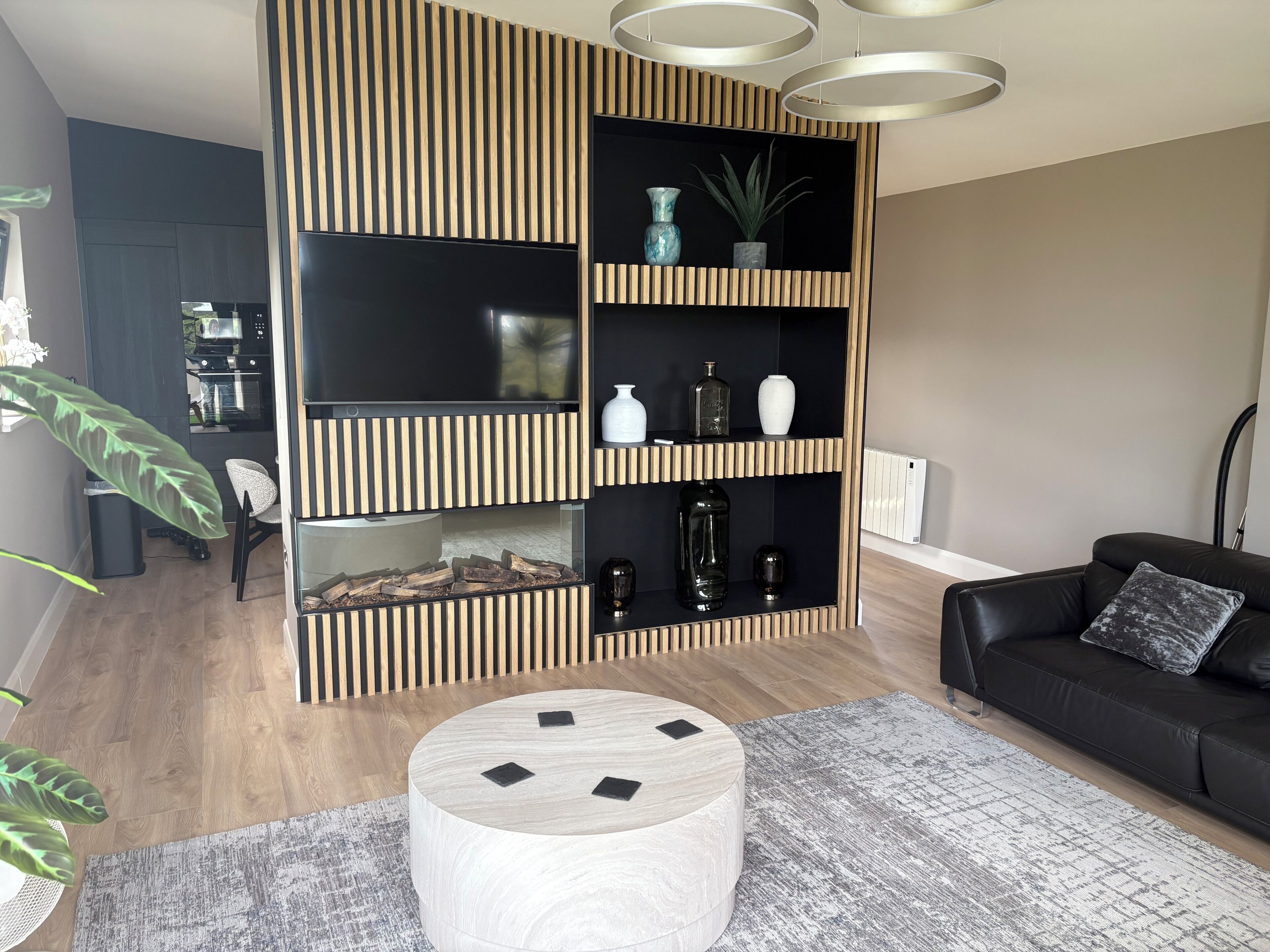 A modern living room with a black entertainment unit, a round wooden coffee table, and a black leather sofa.
