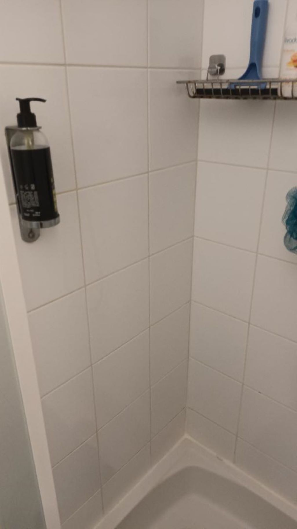 A bathroom with white tiles, a soap dispenser, and a blue toothbrush holder on a shelf.