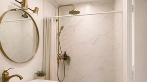Een badkamer met een witte wasbak, een ronde spiegel, een douche met een handdouche en een handdoekrek.