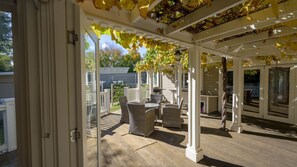 An outdoor patio with wicker furniture, a pergola with yellow leaves, and a view of the backyard. - Cabin Charm—Hot Tub Bliss Moments from the Beach (Cowes)