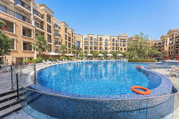 A large, clear blue pool surrounded by lounge chairs and umbrellas, with a multi-story building in the background. - Classy Studio in Al Barsha South that Sleeps 2 (Dubai)
