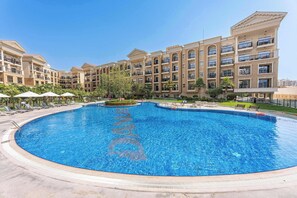 A large swimming pool with a fountain in the center, surrounded by lounge chairs and umbrellas. - Classy Studio in Al Barsha South that Sleeps 2 (Dubai)