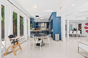 A modern kitchen with white cabinets, a central island, and a dining area with a round table and chairs. - Vibrant Art-Filled Pool Gem near Beach & Las Olas! (Fort Lauderdale)