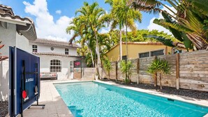 A swimming pool with a wooden fence, palm trees, and a building with a tiled roof. - Vibrant Art-Filled Pool Gem near Beach & Las Olas! (Fort Lauderdale)