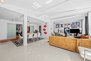 A modern living room with a sofa, a dining area with chairs, and a TV. - Vibrant Art-Filled Pool Gem near Beach & Las Olas! (Fort Lauderdale)