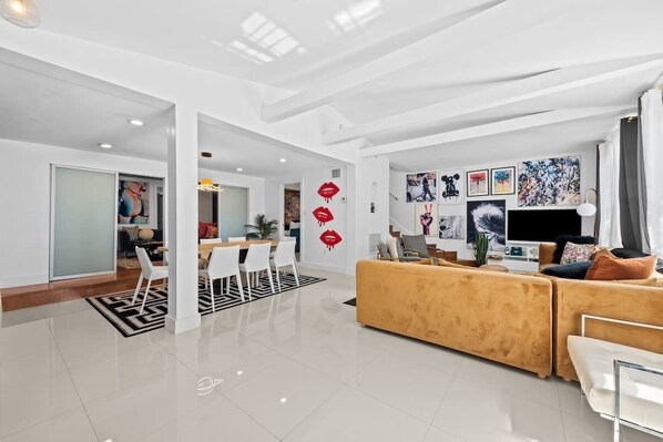 A modern living room with a sofa, a dining area with chairs, and a TV. - Vibrant Art-Filled Pool Gem near Beach & Las Olas! (Fort Lauderdale)