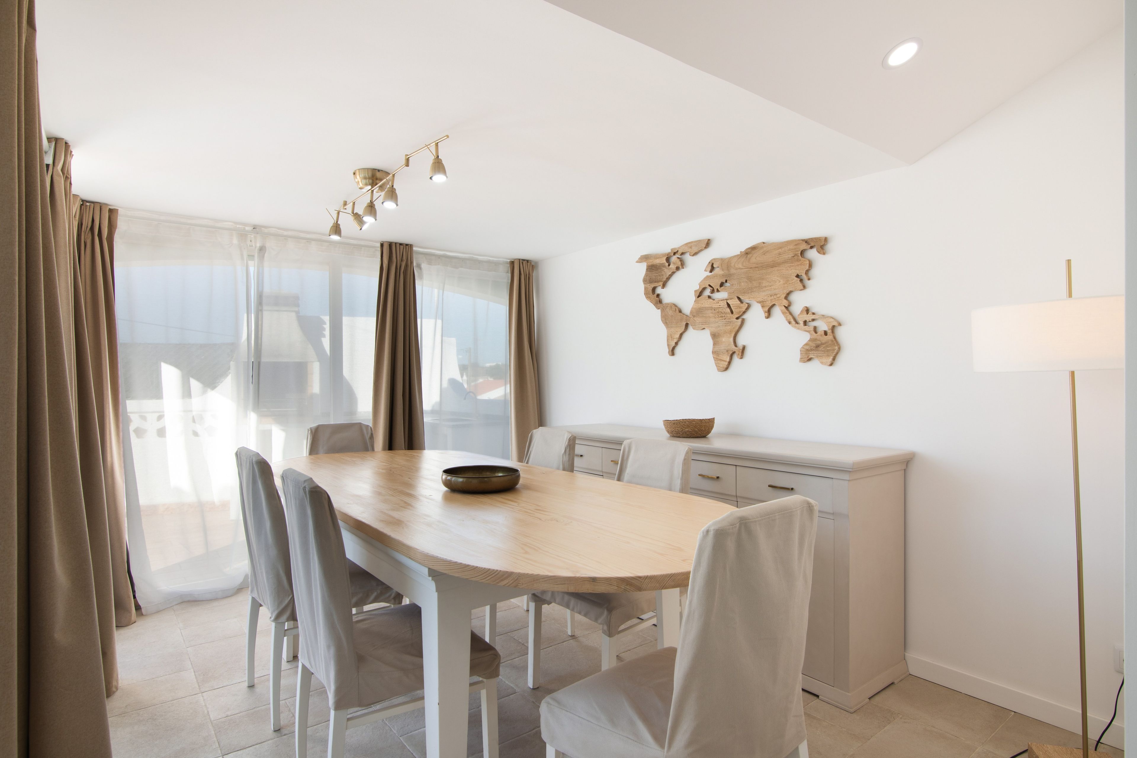 A modern dining room with a wooden table, chairs, a world map wall art, and a kitchen area with a white cabinet.