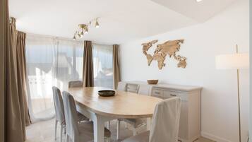 A modern dining room with a wooden table, chairs, a world map wall art, and a kitchen area with a white cabinet.